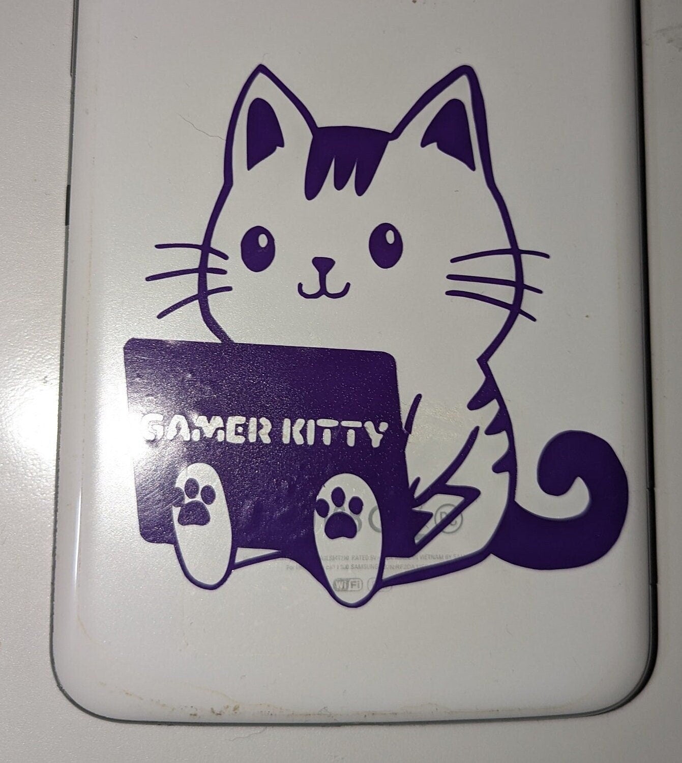 Cute cartoon cat sticker in purple vinyl. The cat is outlined with a solid tail. The cat is holding a laptop that has the words, &quot;Gamer Kitty&quot; in a single line across the middle.